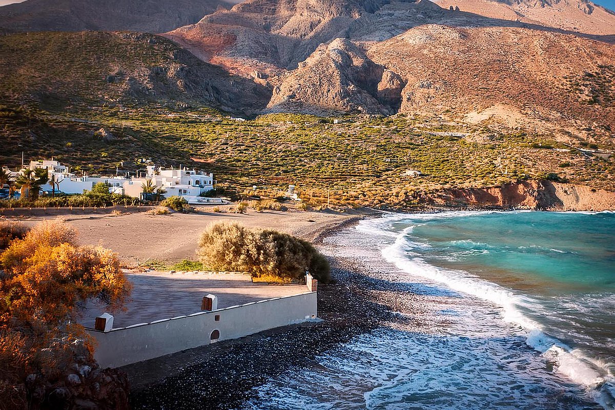 Scenic beach in Crete with gentle waves, rocky mountains, and white buildings in the background.