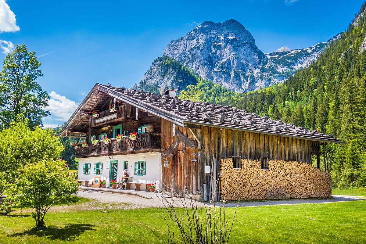 A traditional wooden house in Graubünden, Switzerland, surrounded by trees and mountains under a blue sky with clouds.