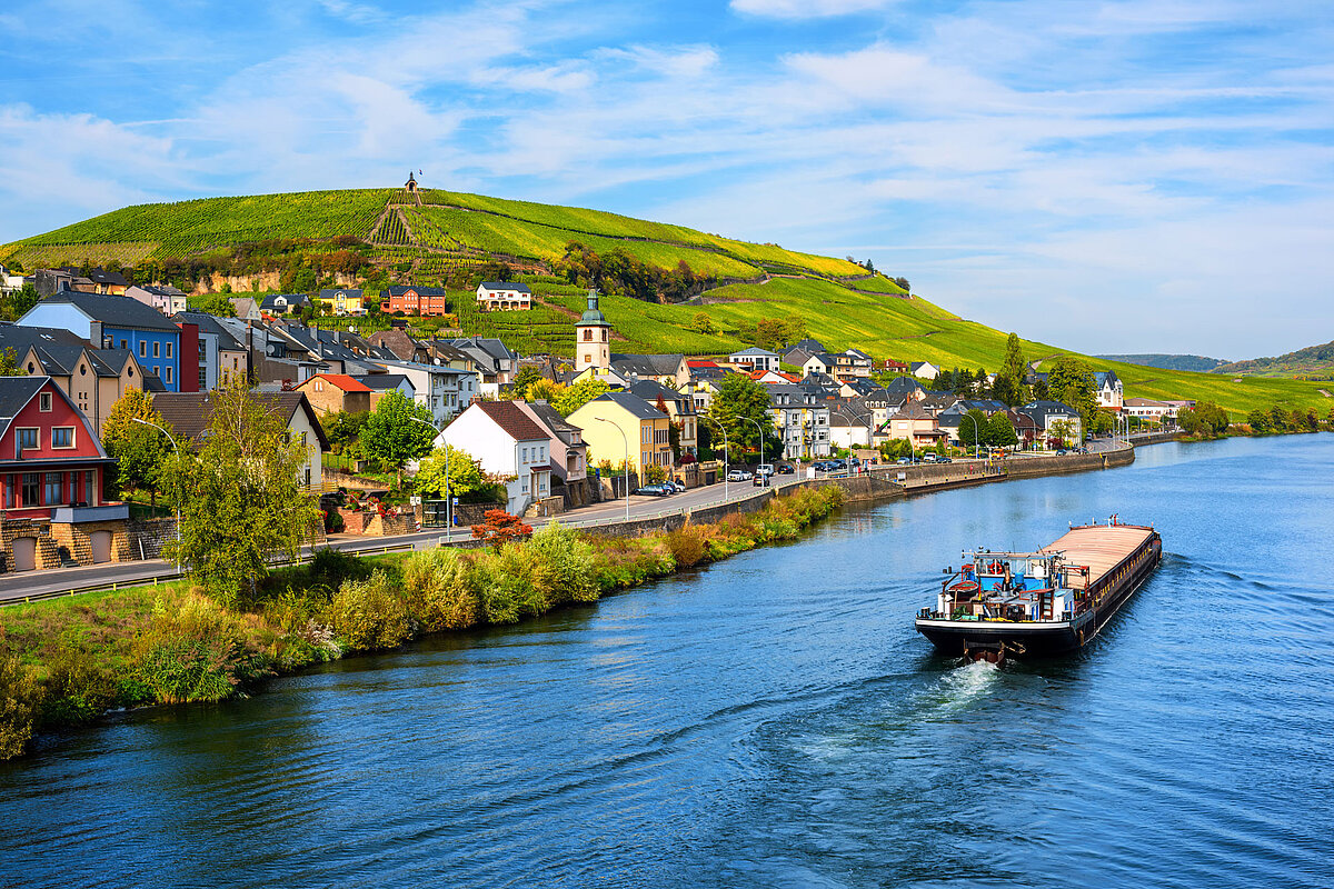 A boat crosses the Moselle River skirting a typical Luxembourg landscape.