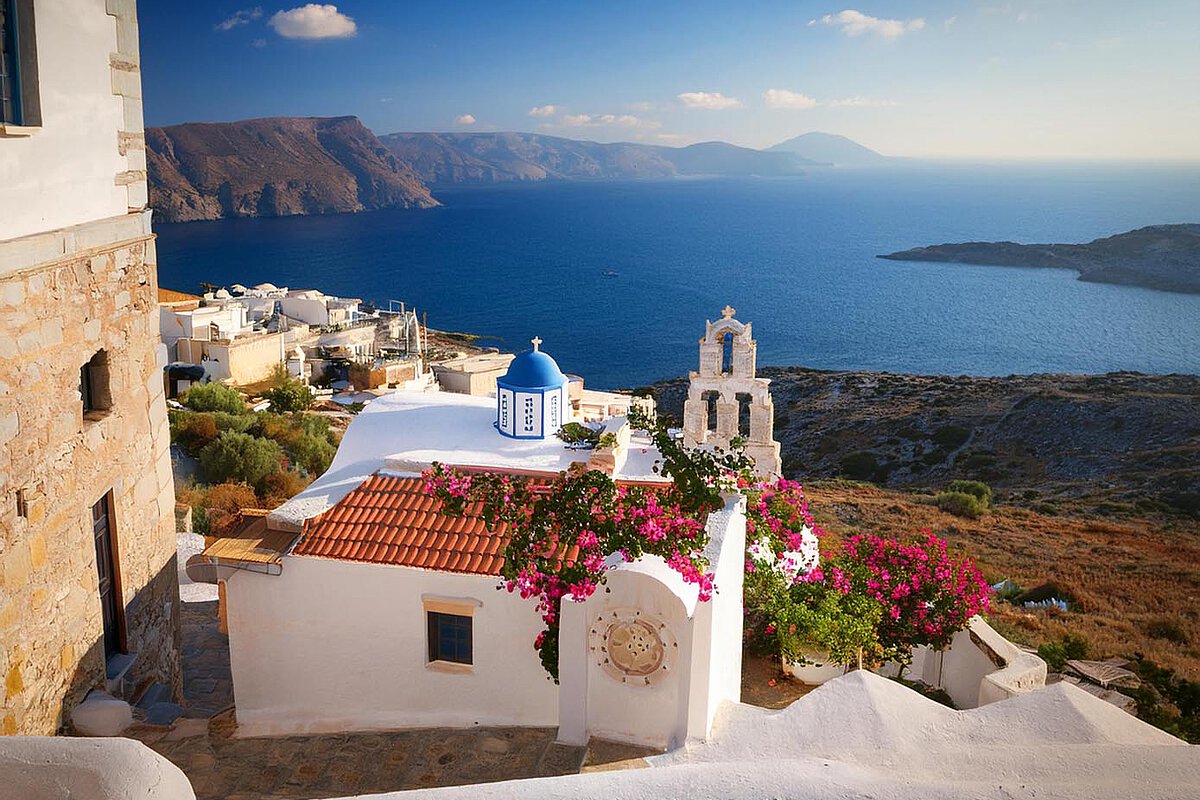 Charming scene in Crete with whitewashed buildings, a blue-domed church, and vibrant flowers overlooking the sea and mountains.