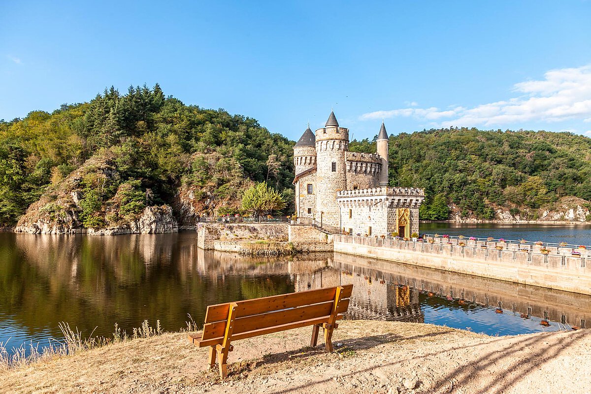 Castle in the Loire Valley with a tranquil lake and greenery, featuring a wooden bench in the foreground.
