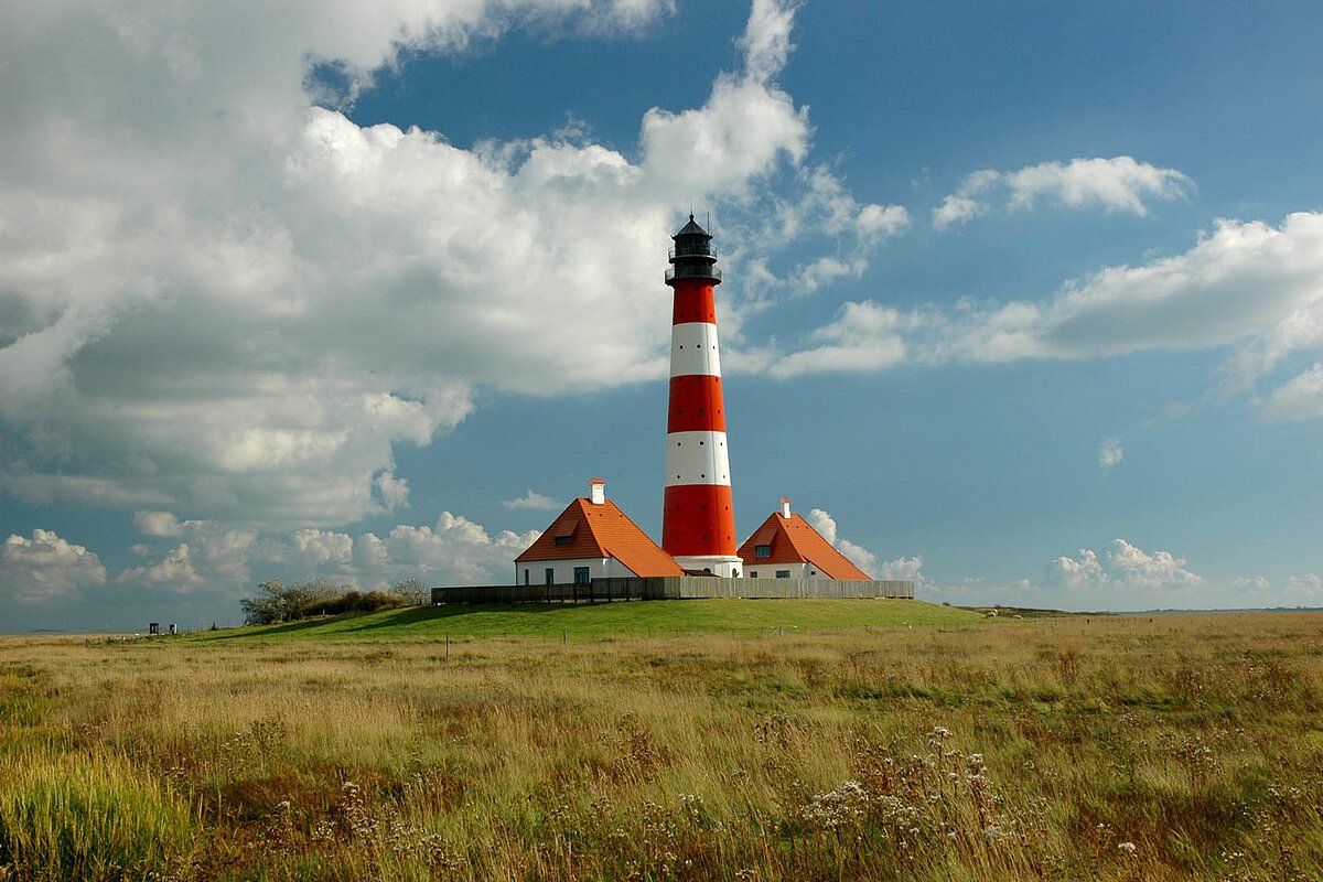 Gestreifter Leuchtturm in Mitteljütland, Dänemark, mit roten und weißen Farben, vor einem bewölkten Himmel und einer grasbewachsenen Landschaft.