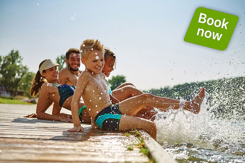 Family with children sitting on a wooden jetty, splashing their feet in the lake. Summer holiday in the Bavarian countryside