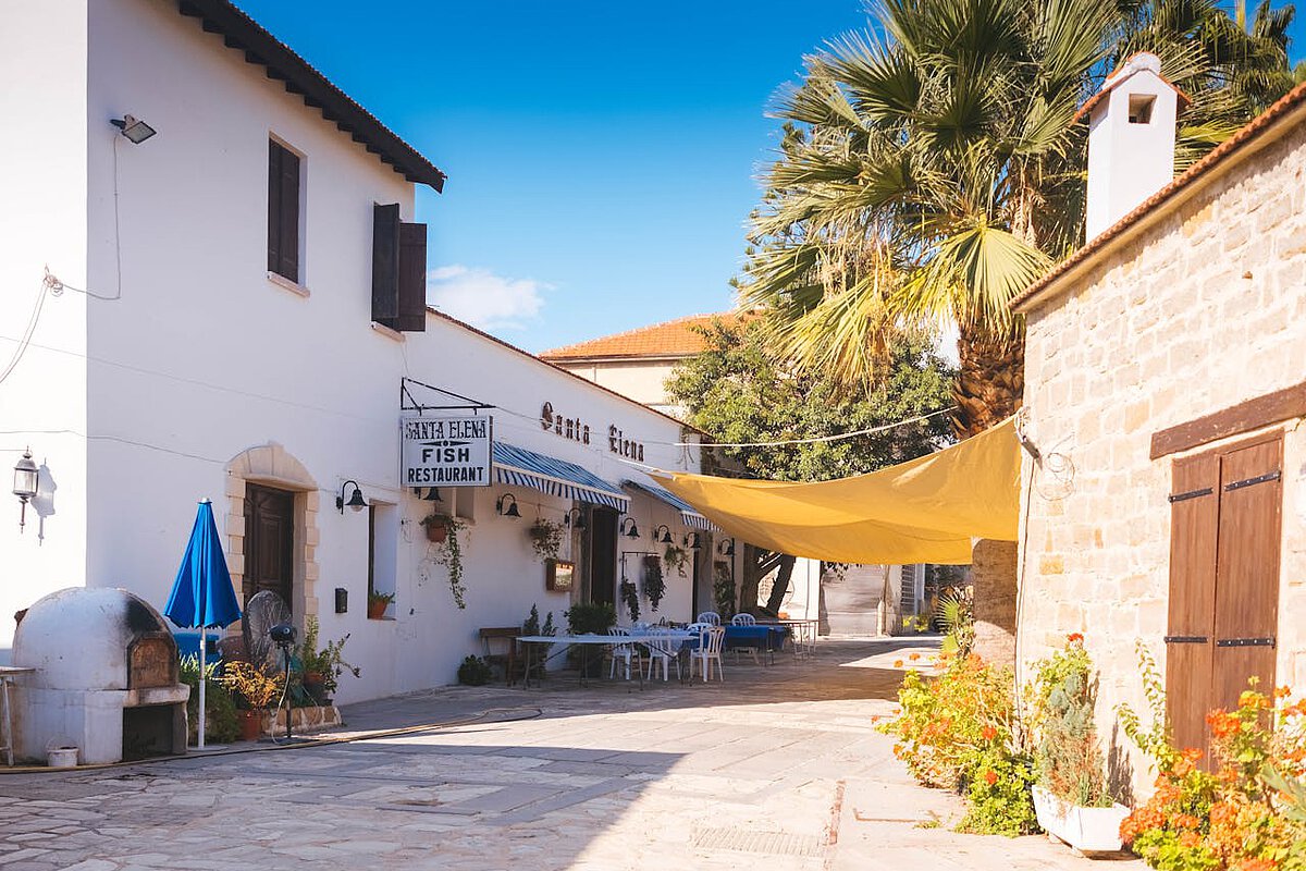 A typical Cyprus village, sun-kissed during the summer. You can see the entrance to a bar with chairs outside.