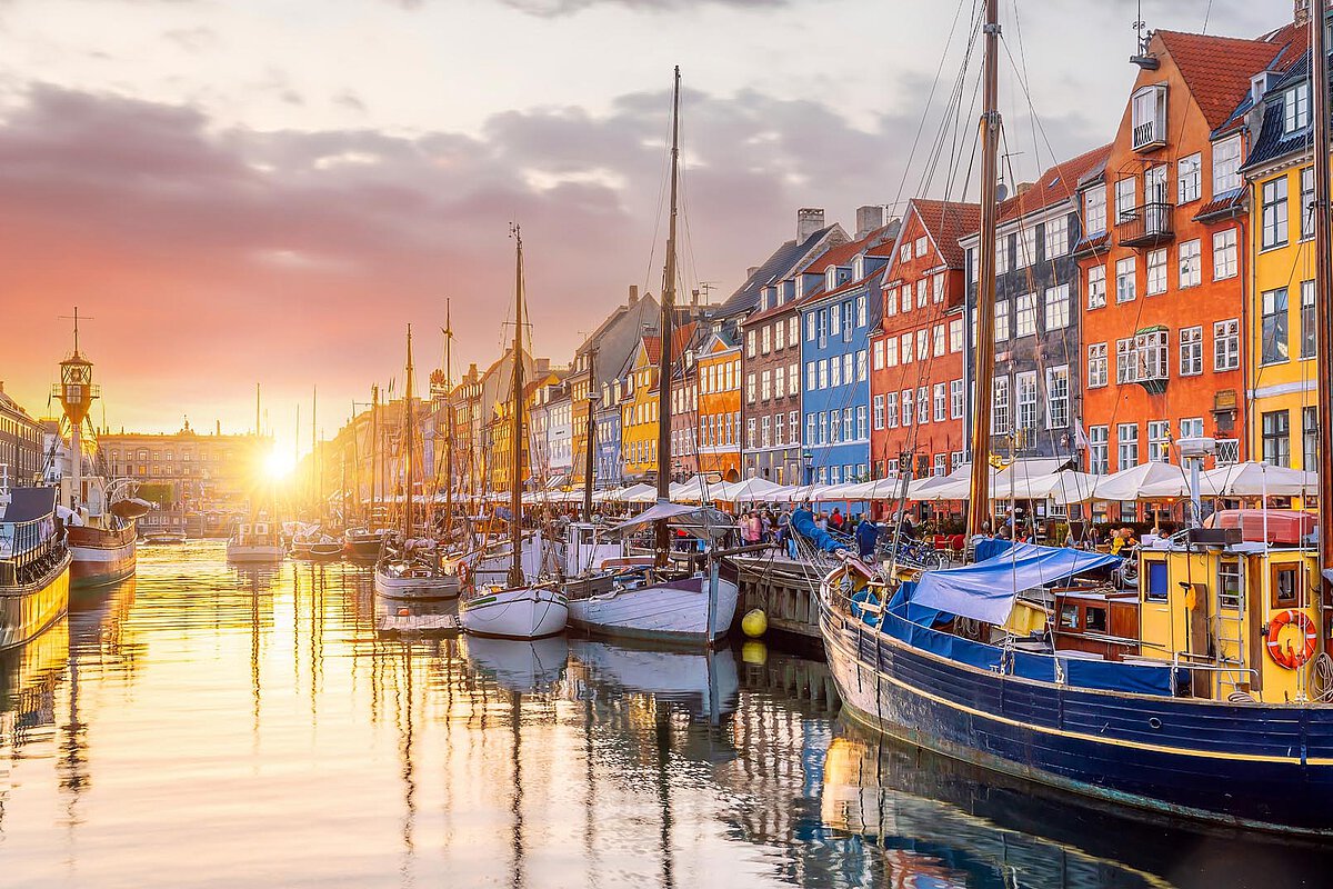 Colorful buildings and boats along the canal at Nyhavn in Copenhagen, Denmark, illuminated by sunset.