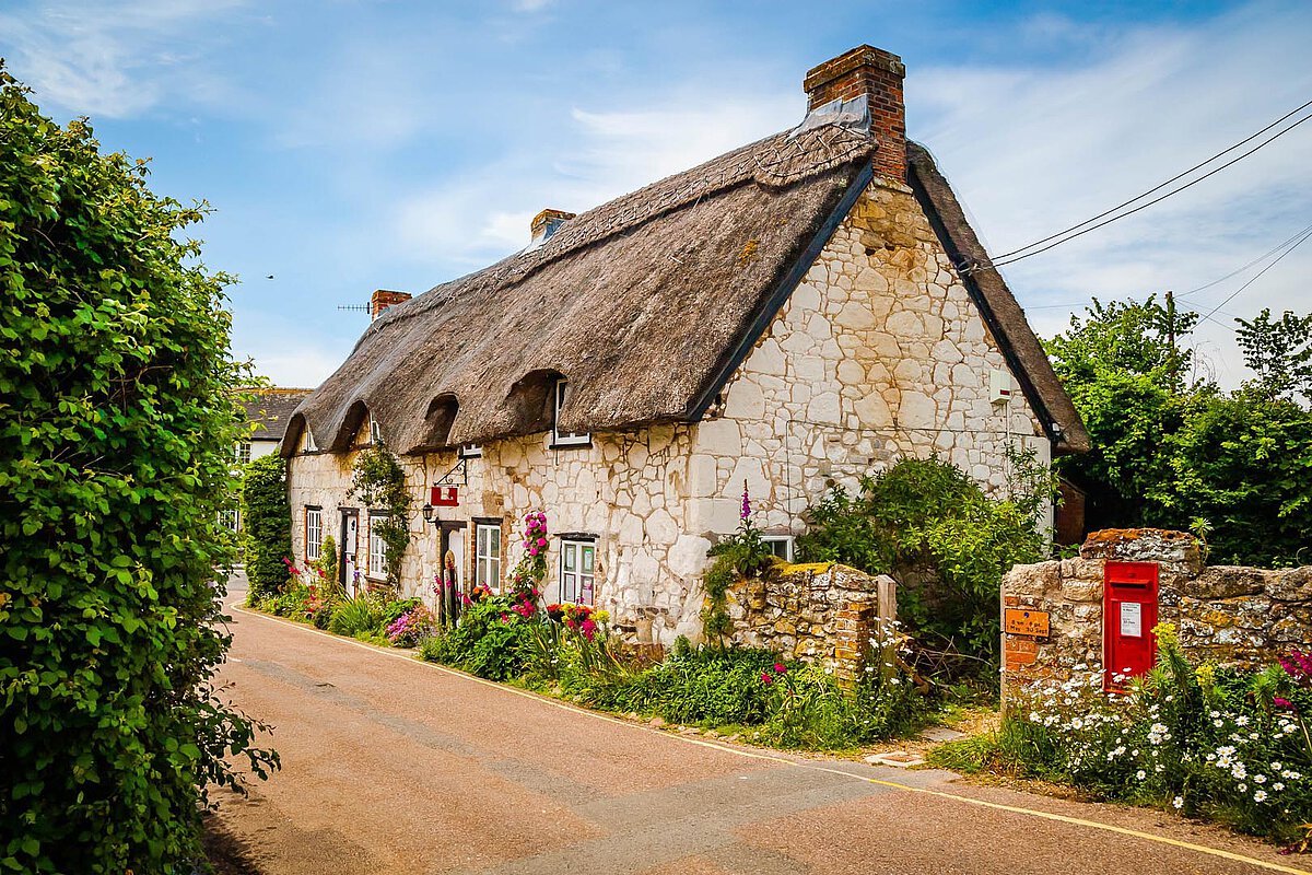 Malerisches Reetdachhaus auf der Isle of Wight, gelegen an einer ruhigen Straße, umgeben von üppigem Grün und lebhaften Blumen.