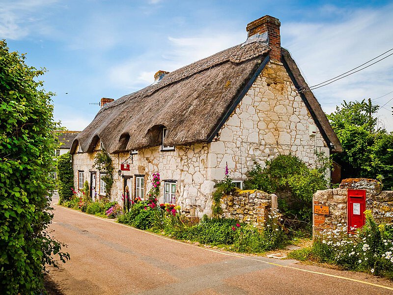 Malerisches Reetdachhaus auf der Isle of Wight, gelegen an einer ruhigen Straße, umgeben von üppigem Grün und lebhaften Blumen.