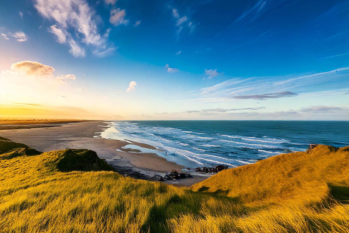 A panoramic view of the Northern Sea with sandy shores and rolling waves under a colorful sky.