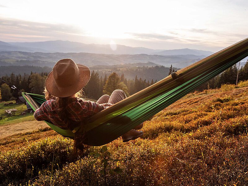Woman with a hat relaxing in a hammock overlooking an autumn mountain landscape.