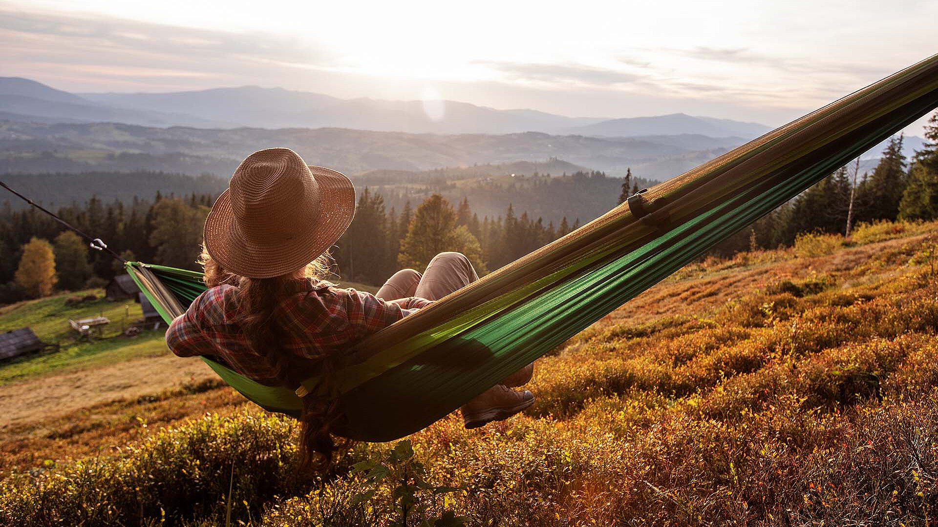 Woman with a hat relaxing in a hammock overlooking an autumn mountain landscape.