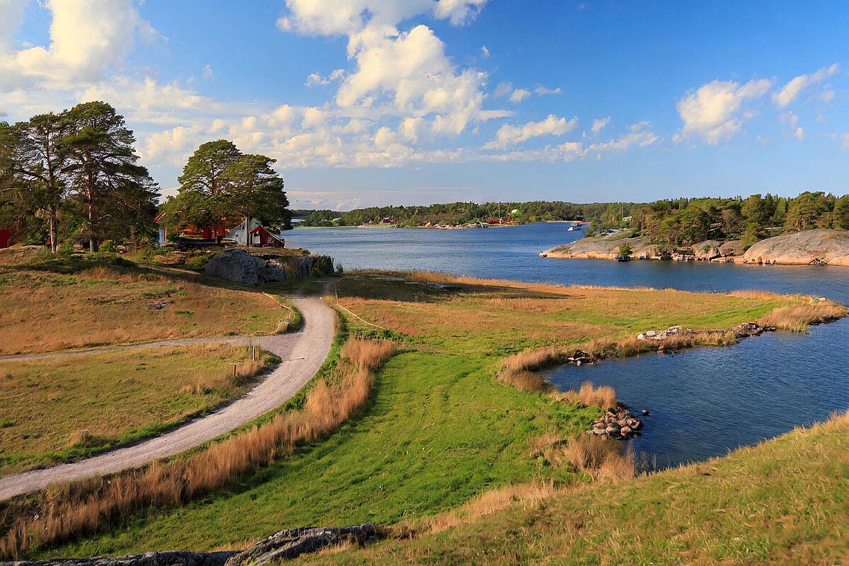 A scenic landscape in Halland, Sweden, with a winding path through greenery, a tranquil waterway, and distant boats, showcasing the area's natural beauty.