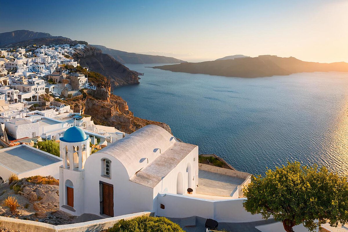 Beautiful view of a Greek island with white buildings, a blue-domed church, and calm waters during sunset.