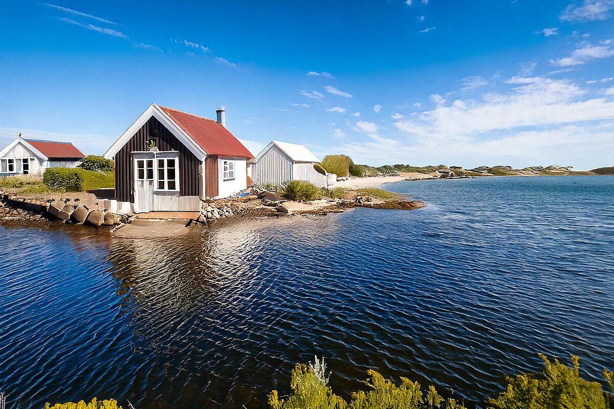Coastal house with a red roof by the water in Denmark, surrounded by greenery.