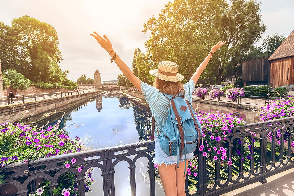 Person with a backpack enjoying the view from a bridge in Picardy, surrounded by flowers and water.