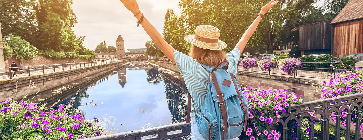 Person with a backpack enjoying the view from a bridge in Picardy, surrounded by flowers and water.