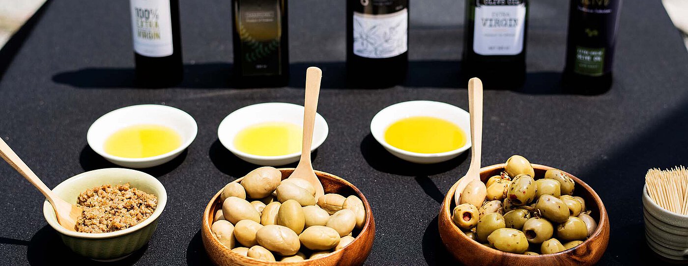 Tasting table with small bowls of olive oil, bowls of olives, and several olive oil bottles in the background.